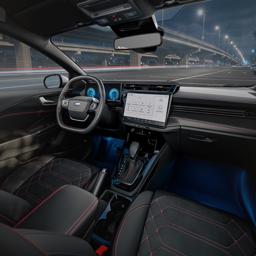 Interior of a Ford Puma at night, showing the steering wheel, large touchscreen, and gear shifter.