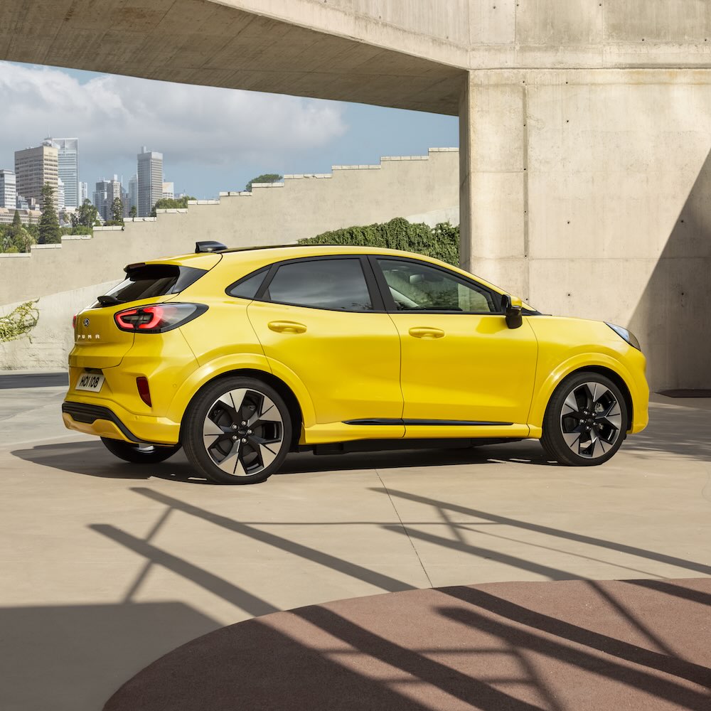  Side view of a yellow Ford Puma parked on a paved surface in front of a modern building.