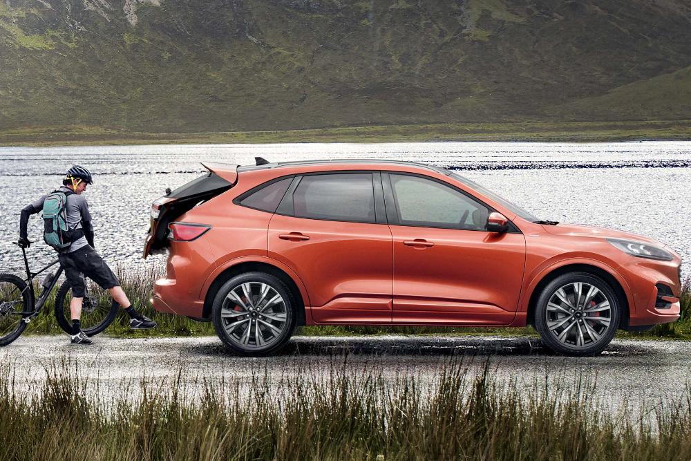 An orange Ford Kuga parked beside a lake, with a cyclist loading a bike into the open boot.