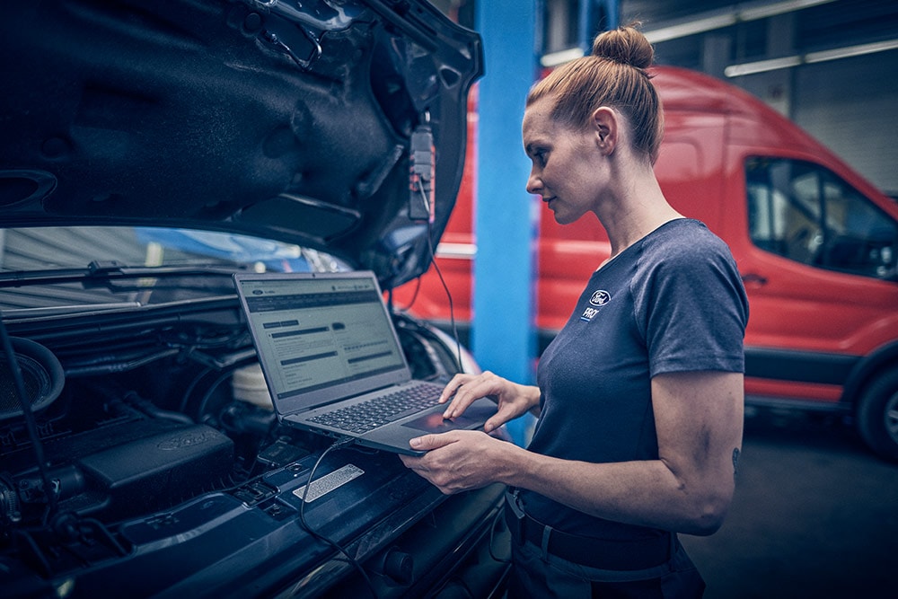 Technician looks under the hood with laptop.