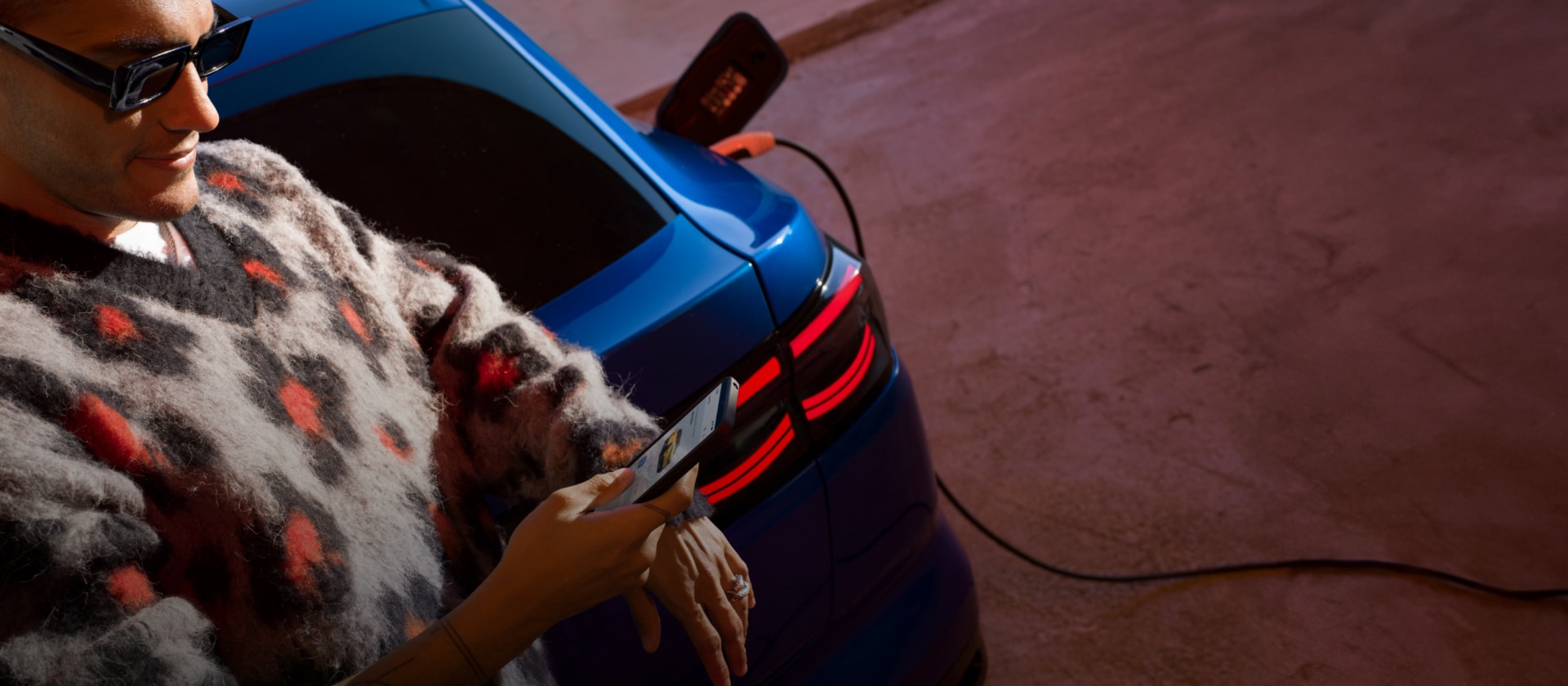 A person charging a blue Ford Capri EV at a public charging station. 