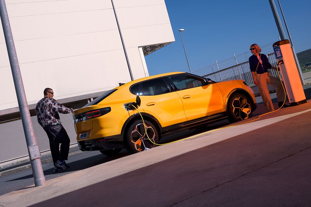 People charging a yellow Ford Capri EV at a public charging station. 