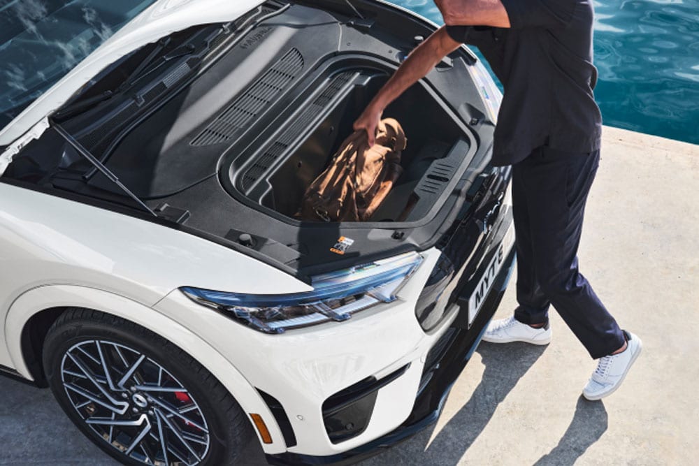 A person placing a holdall bag into the frunk of a white Ford Mustang Mach-E electric car. 