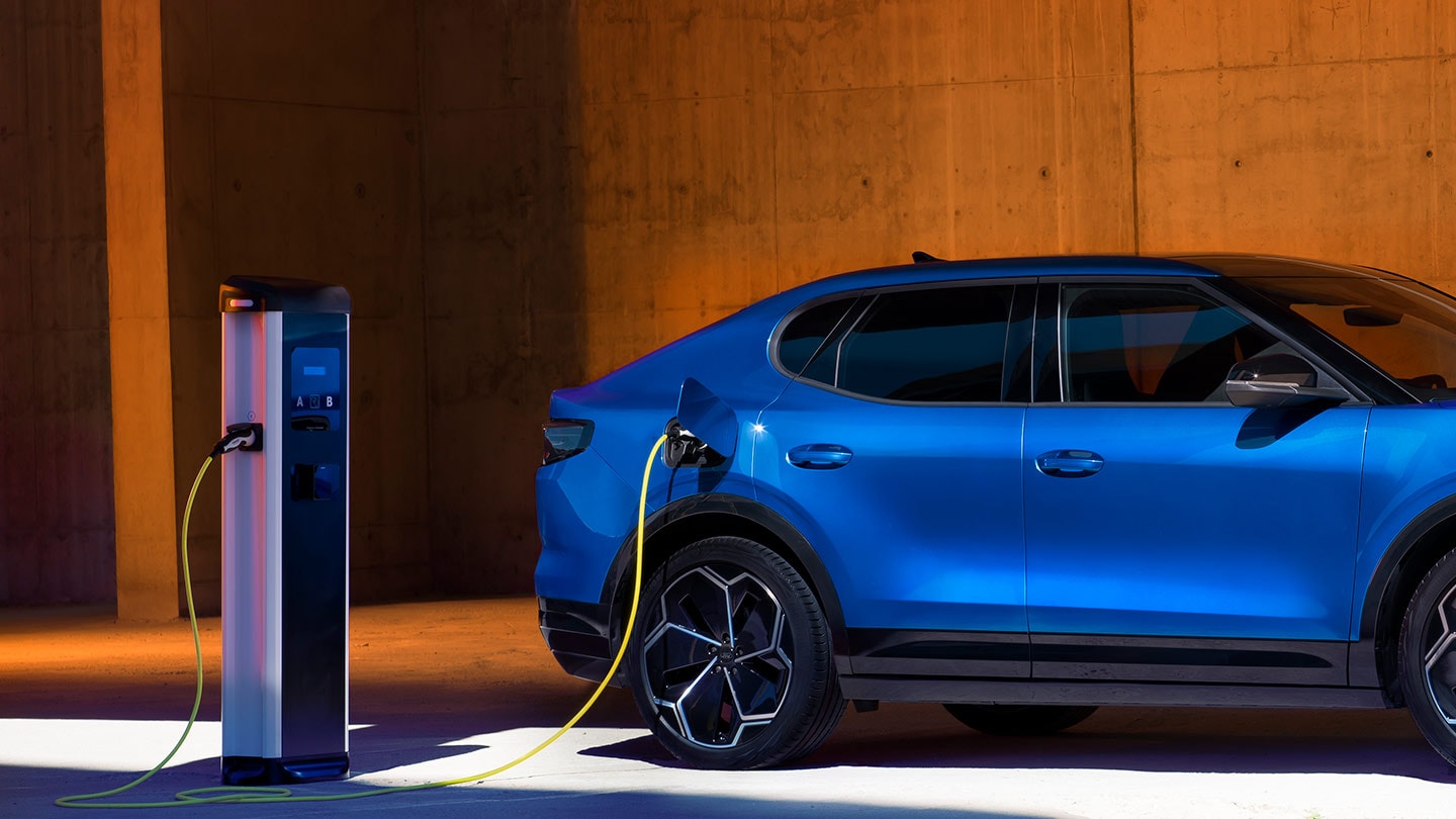 A blue Ford Capri eletric vehicle plugged in to an EV charger. 