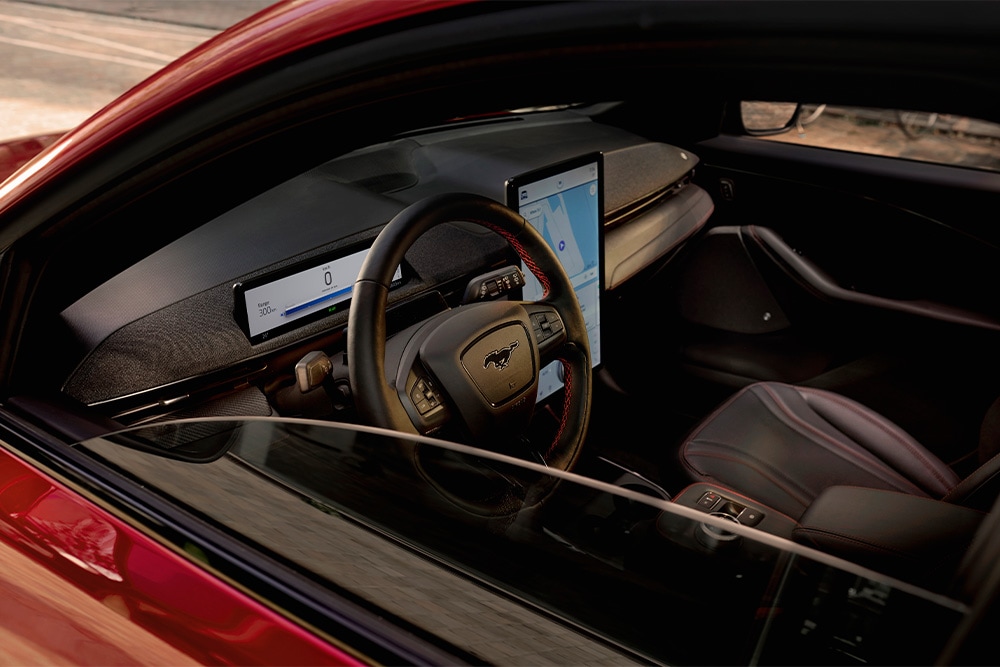 Interior of a red Mach-E with black leather seats, a digital dashboard and a large touchscreen.