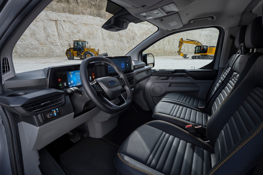  The interior of a Ford E-Transit Custom electric van, showing the seats and steering wheel, parked in a quarry. 