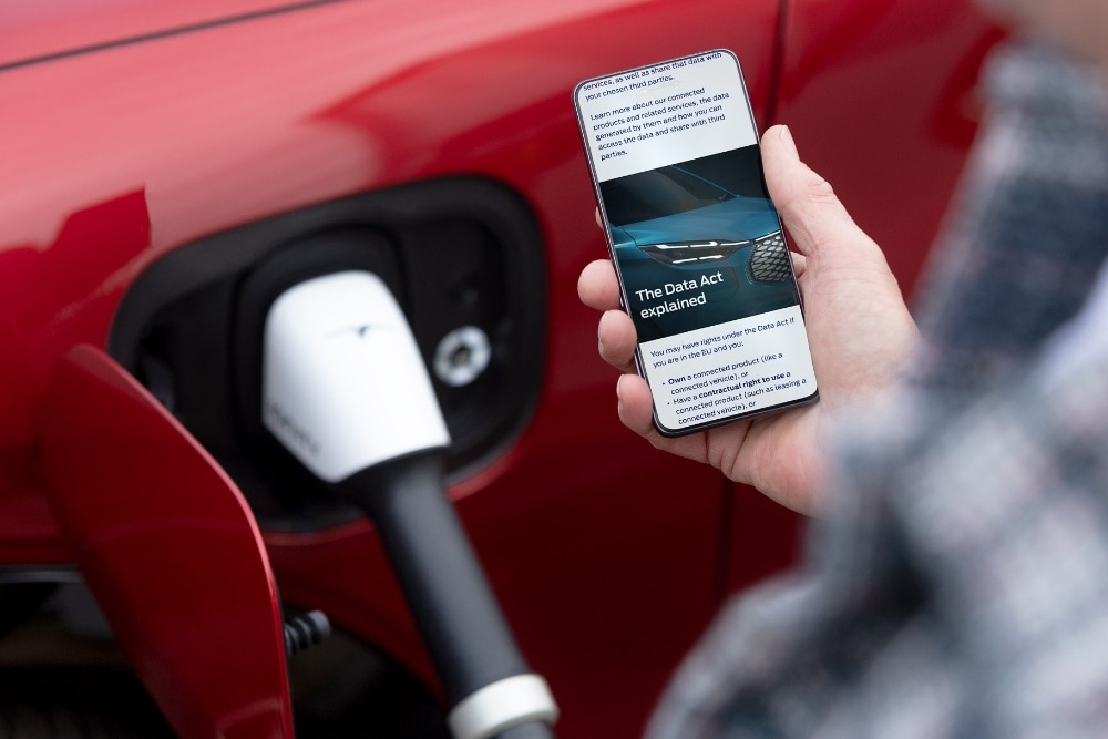 A person reading an explainer on the EU Data Act on their phone next to a charging electric vehicle.