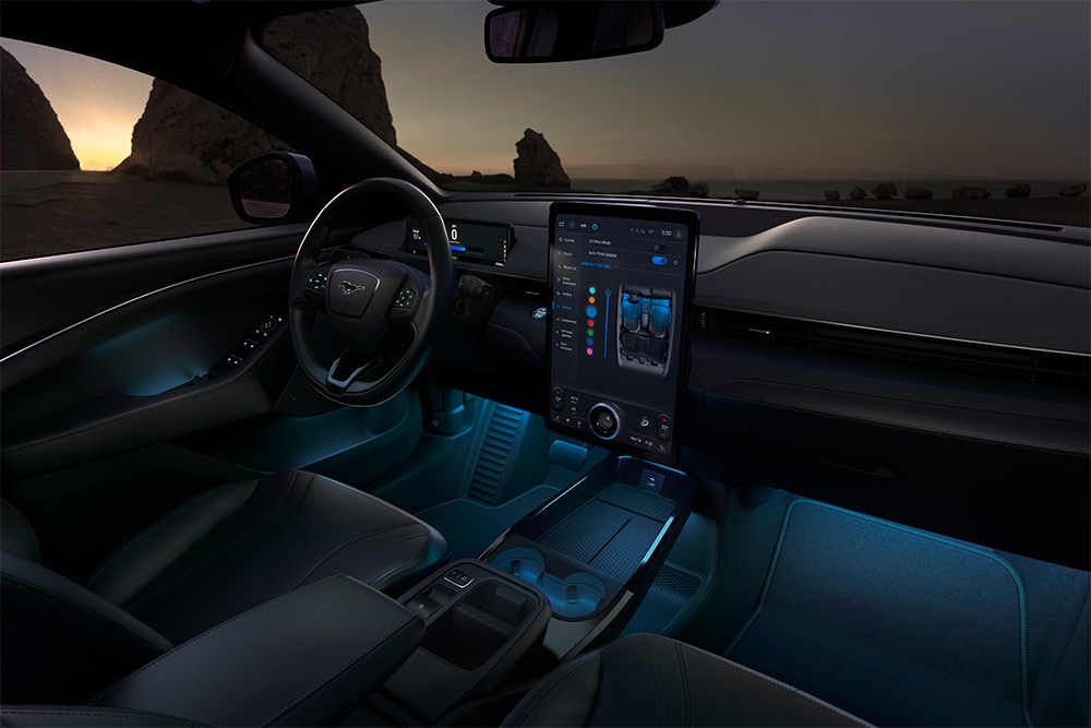 The interior of the Ford Mustang Mach-E at night, showing the 15.5" SYNC 4 touchscreen and ambient LED lighting set to blue.