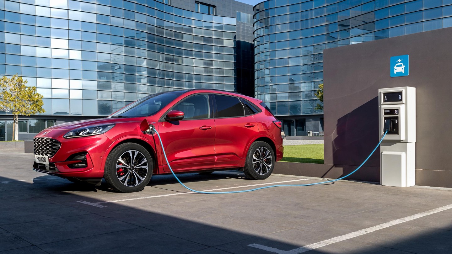 Red Ford Kuga charging at a public charging point in front of office buildings