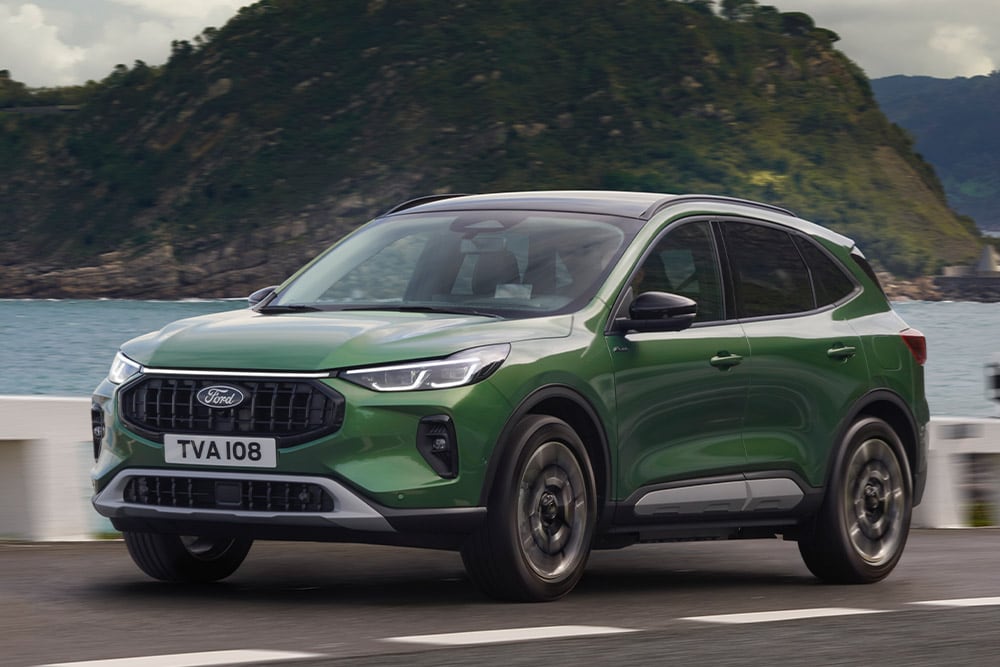 A green Ford Kuga driving along a coastal road.