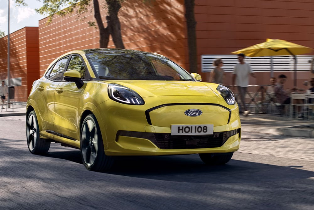 Front view of a yellow electric Ford Puma Gen-E® driving along a city road.