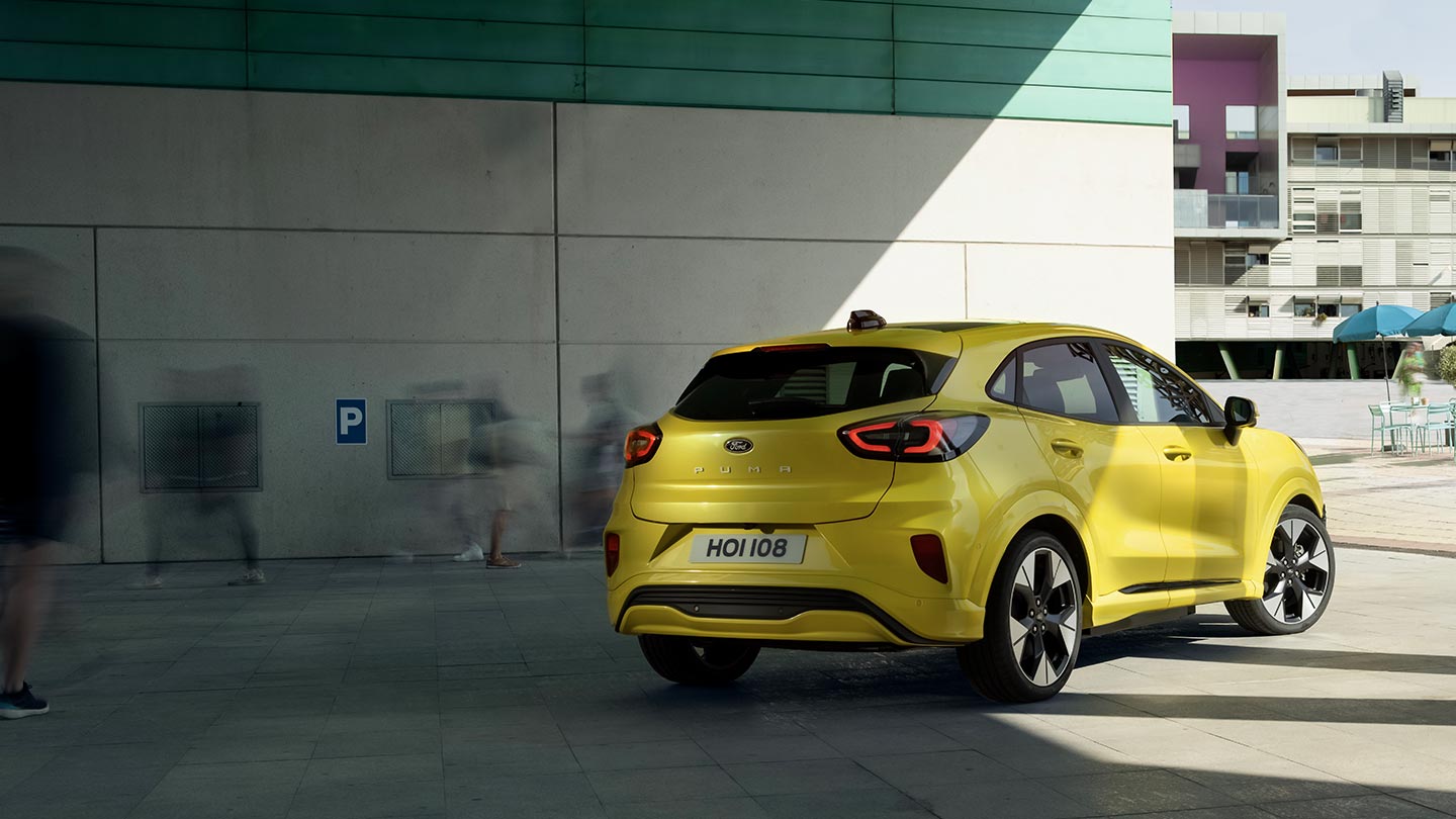 The rear angle of a yellow electric Ford Puma Gen-E® parked under a bridge.