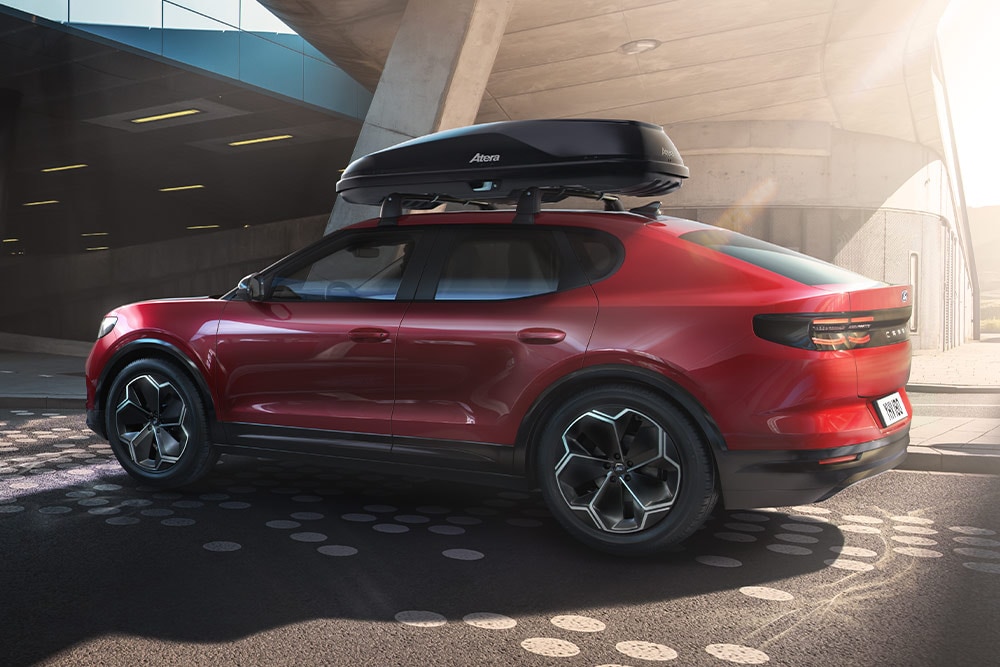 Yellow Ford Capri parked in a modern concrete structure, rear view showing a luggage box attached to the rear with a luggage box carrier.