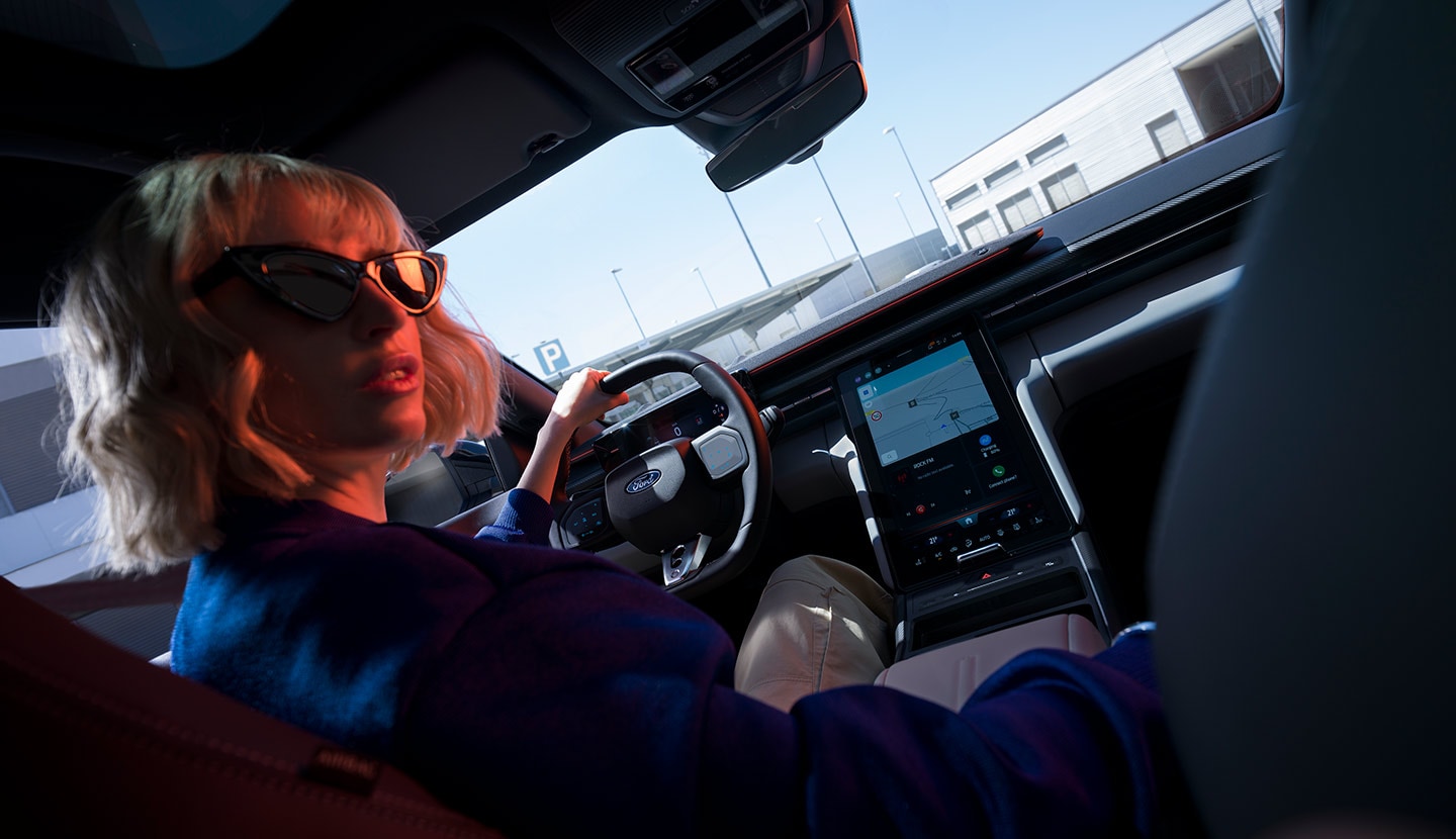 A woman sits in the driving seat of a parked Ford Capri®, with the steering wheel and large SYNC® Move touchscreen visible.