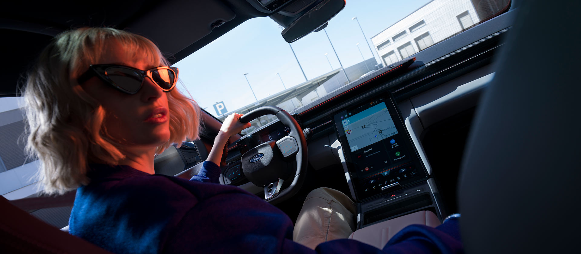A woman sits in the driving seat of a parked Ford Capri®, with the steering wheel and large SYNC® Move touchscreen visible.