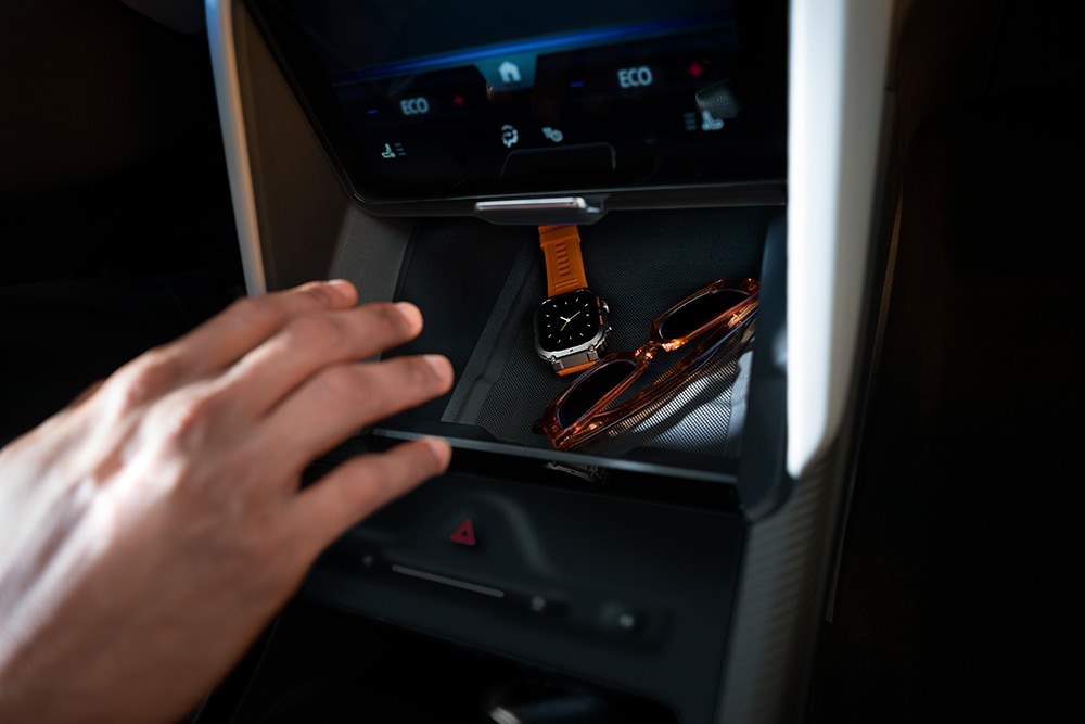 A hand reaches toward the My Private Locker compartment in the Ford Capri®, showing a watch and a pair of sunglasses inside.