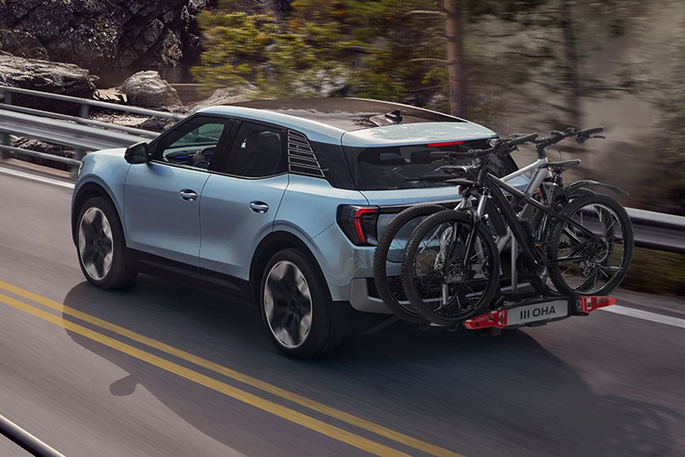 Rear view of a blue Ford Explorer, two bicycles mounted on the back, driving on a winding mountain road.
