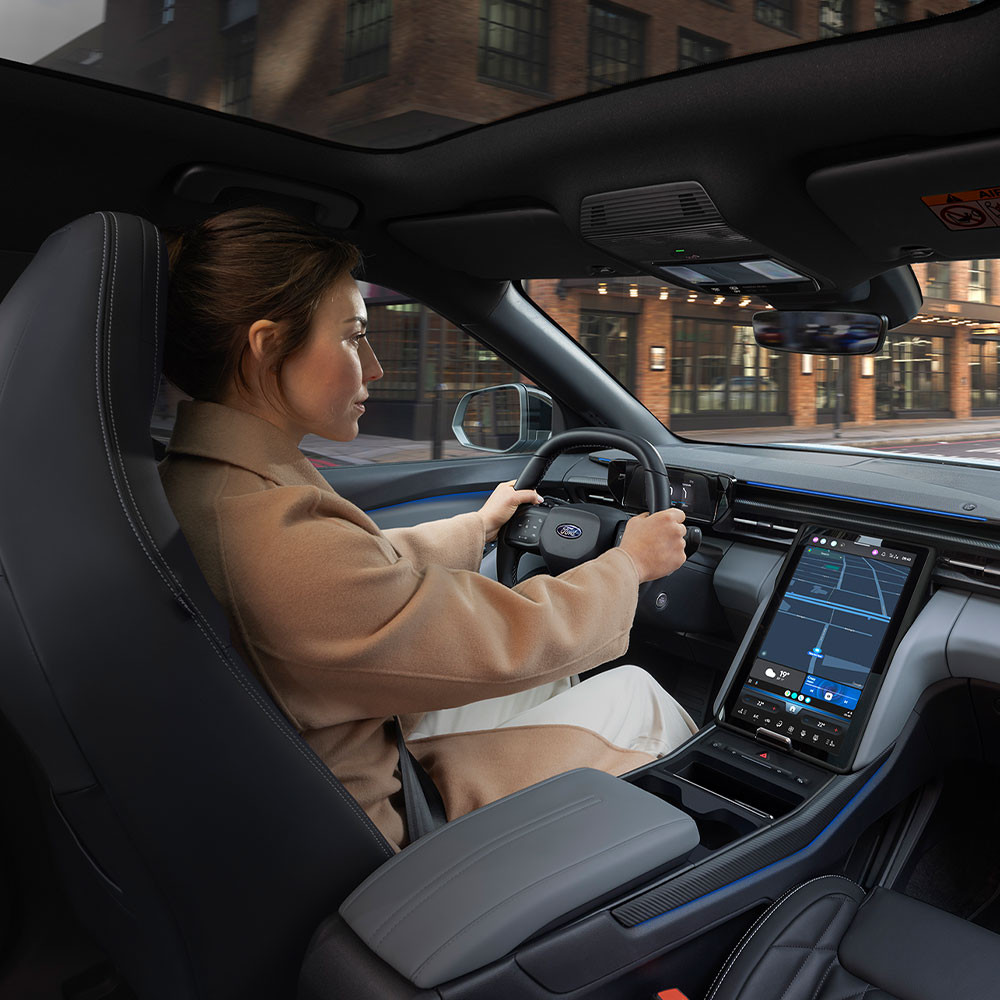 A person driving the electric Ford Explorer through the city, showing the large 14.6" SYNC Move touchscreen.