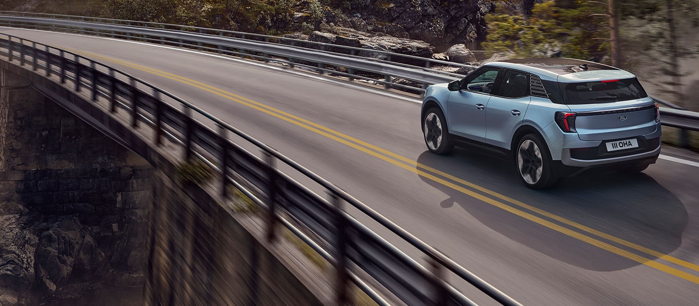 Rear view of a light blue Ford Explorer driving on a road with a mountain backdrop.