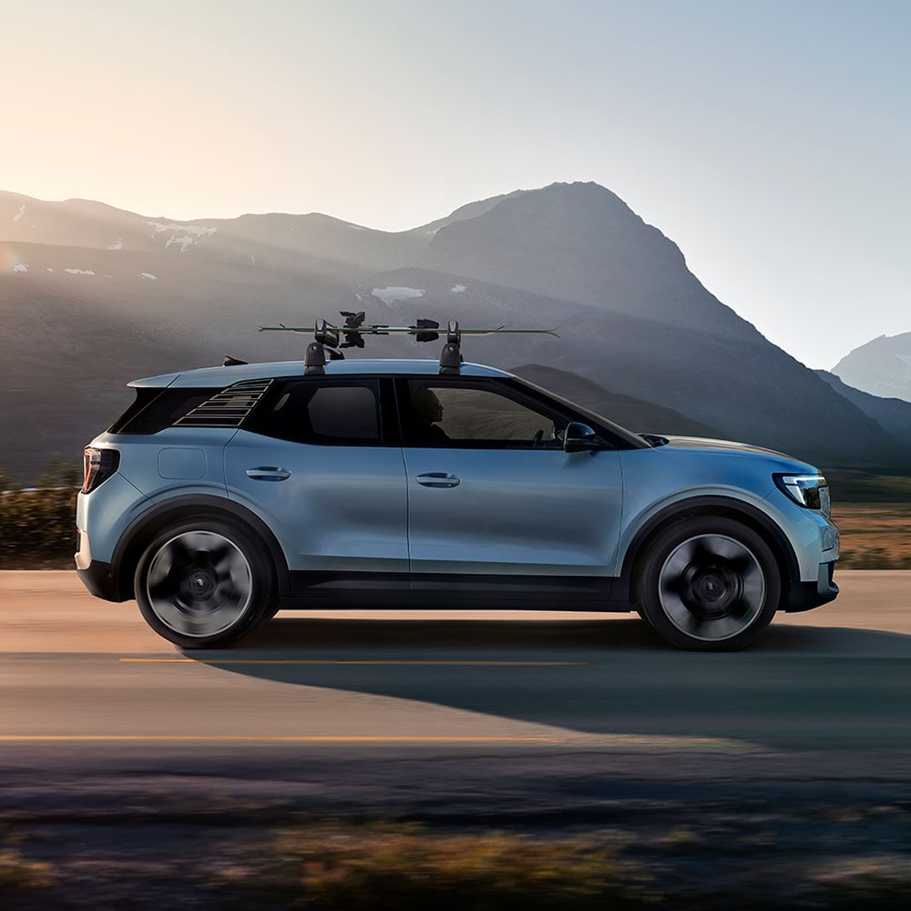 Side view of a blue Ford Explorer with a roof rack driving on a mountain road.