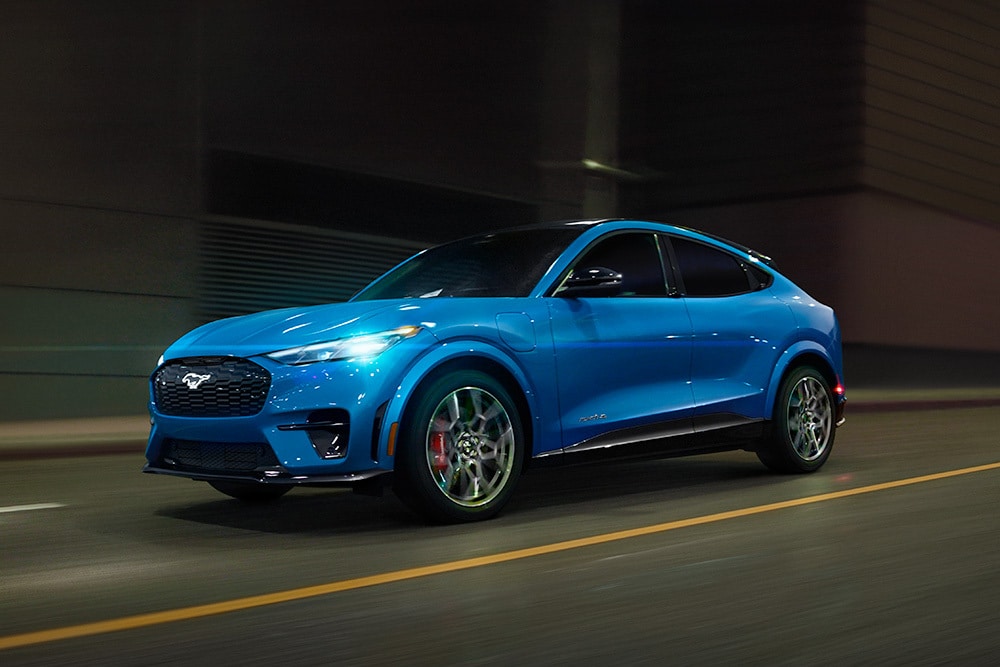 A blue Ford Mustang Mach-E GT electric sportscar driving along an open road.