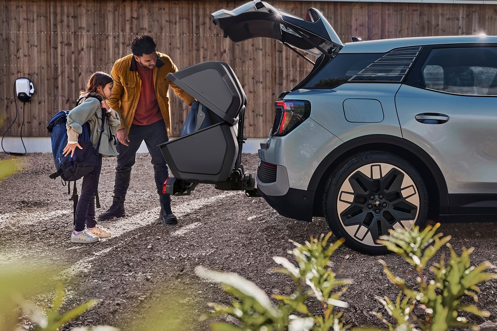A man and child standing by the open boot of a Ford Explorer SUV, loading a folded pushchair.