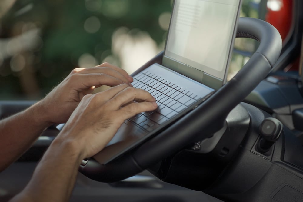 A person's hands are typing on a laptop placed on the fold-flat steering wheel of the Ford Tourneo Custom.