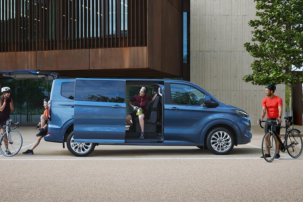 Blue Ford Tourneo Custom van parked with its side doors open and people with bikes nearby.