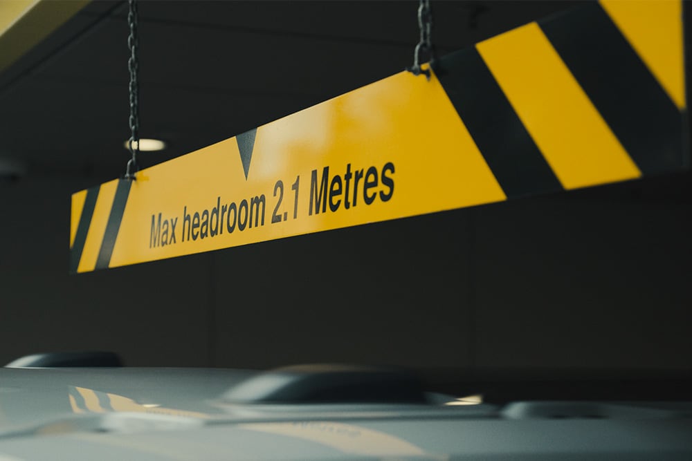 Yellow and black sign in a parking garage reads "Max headroom 2.1 Metres".