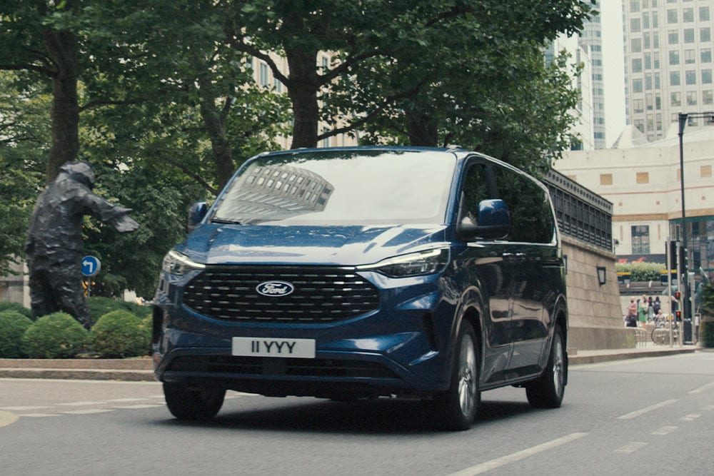 Front 3/4 view of a blue Ford Transit Custom driving on a city street.