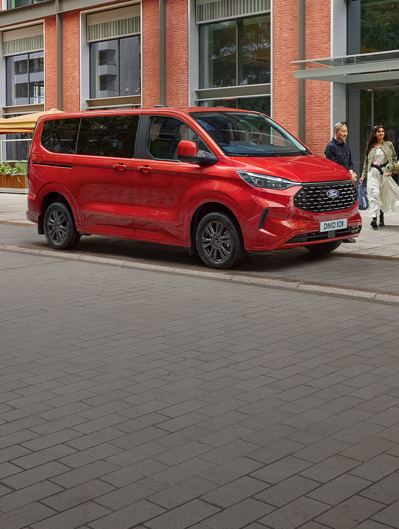 A red Ford Tourneo Custom is parked on a city street. 