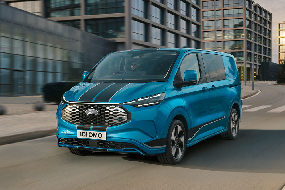 Blue Ford E-Transit Custom Sport Double Cab-in Van with black bumper stripe driving on a city street.
