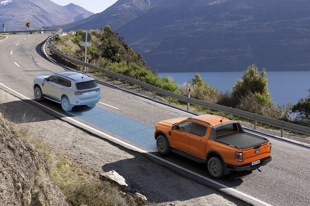 Yellow Ford Ranger Raptor driving along a scenic mountain route, highlighting the vehicle's driver assist systems.