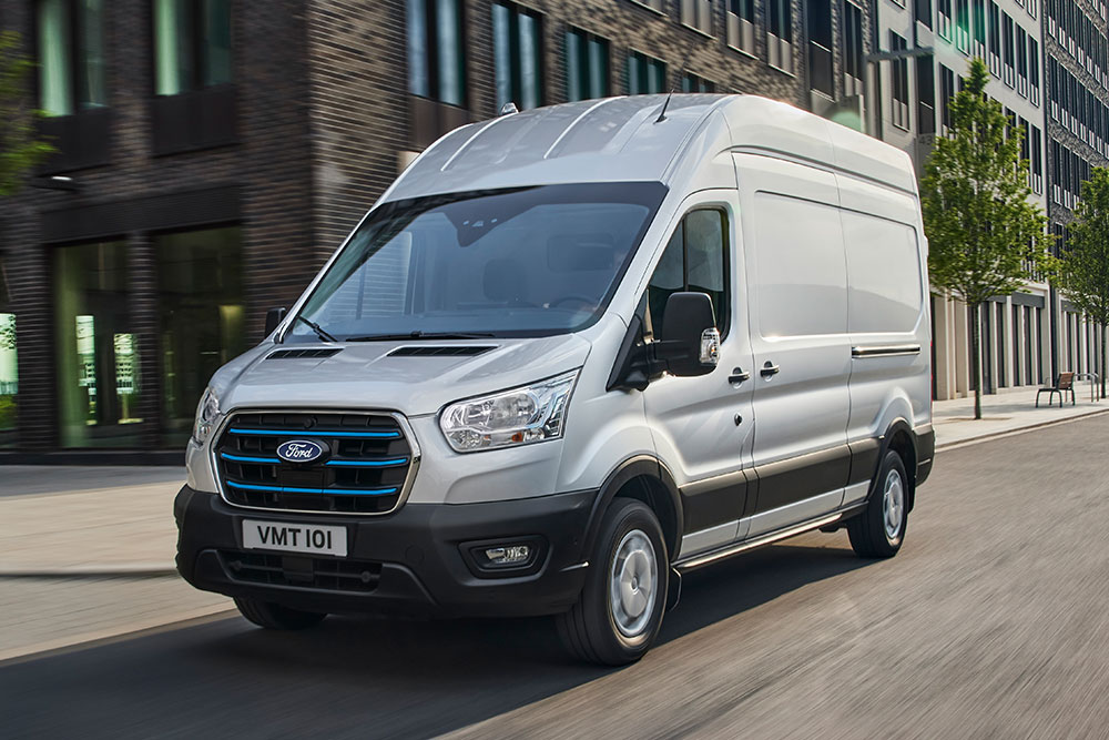 Silver Ford E-Transit electric van driving on a city street.