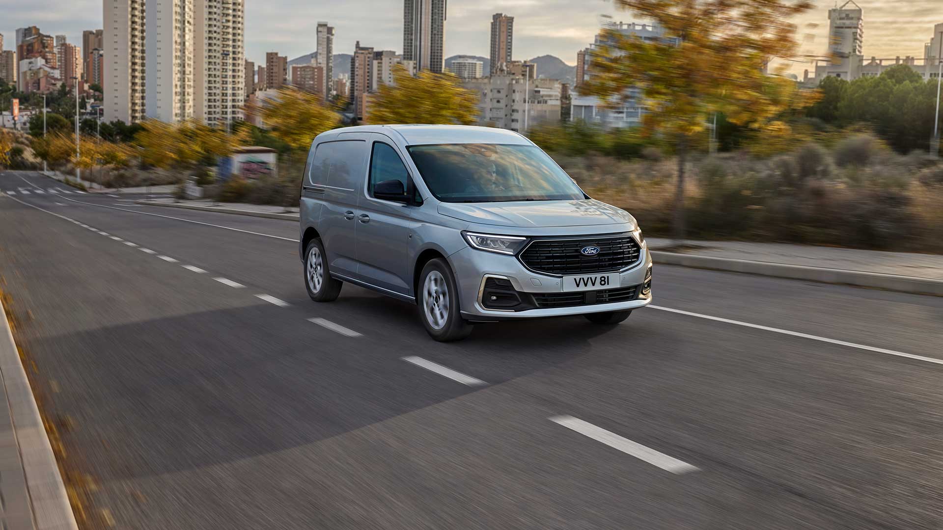 Ford Transit Connect driving in a city, showing chrome exterior fog lamp surrounds and automatic headlights.