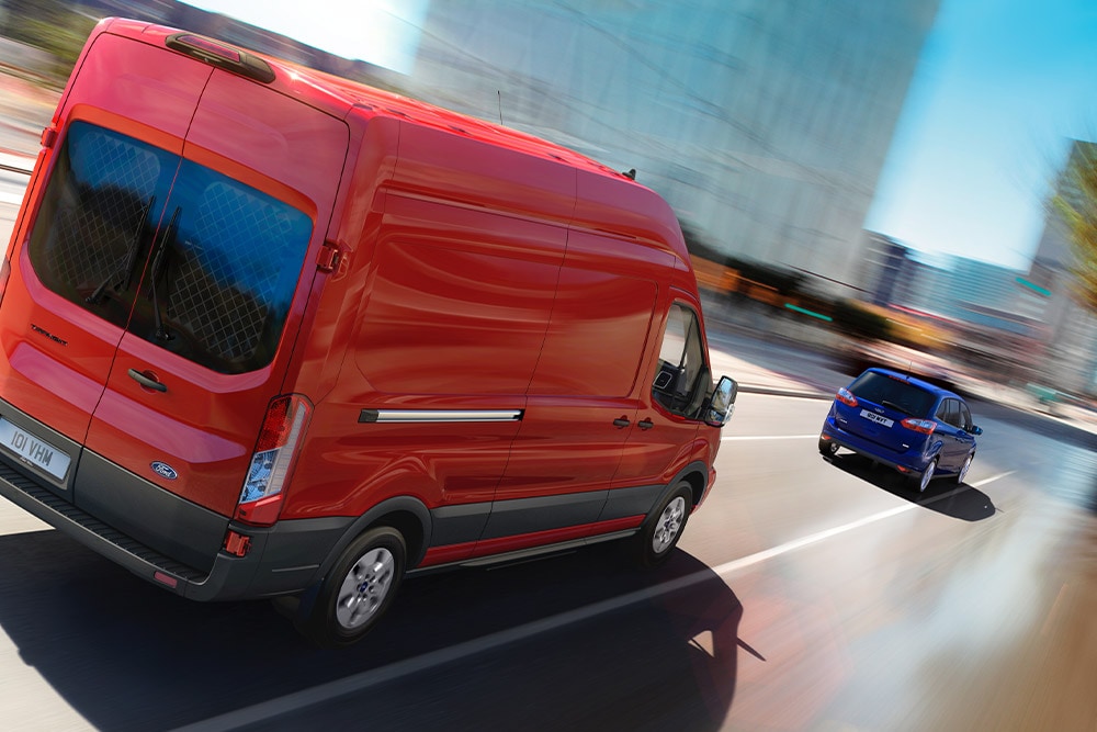 Red Ford Transit Van driving along a city road.