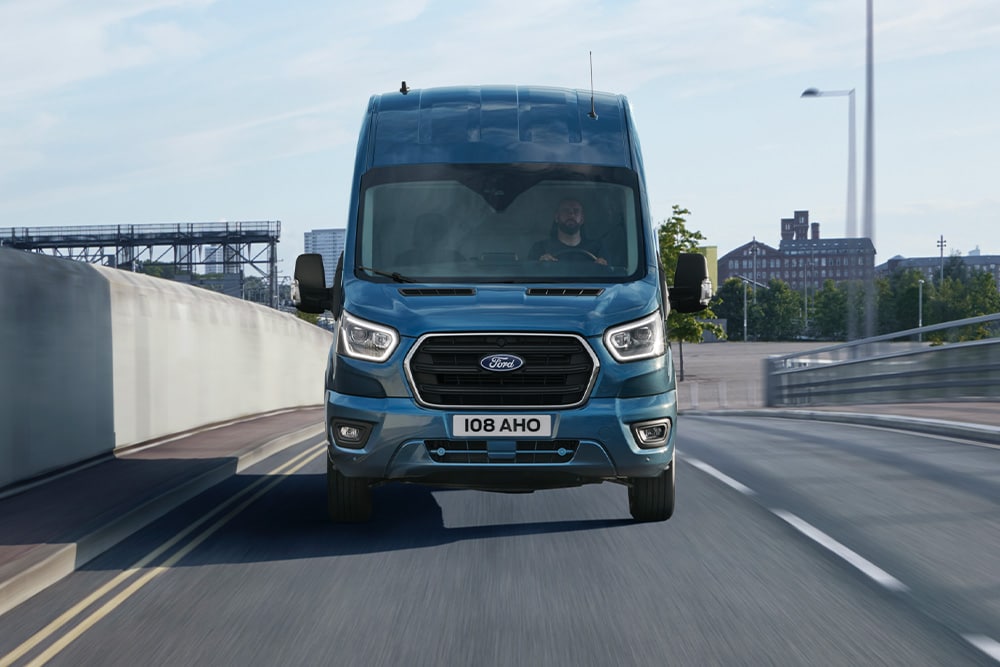  Front view of blue Ford Transit Van driving on a road. 