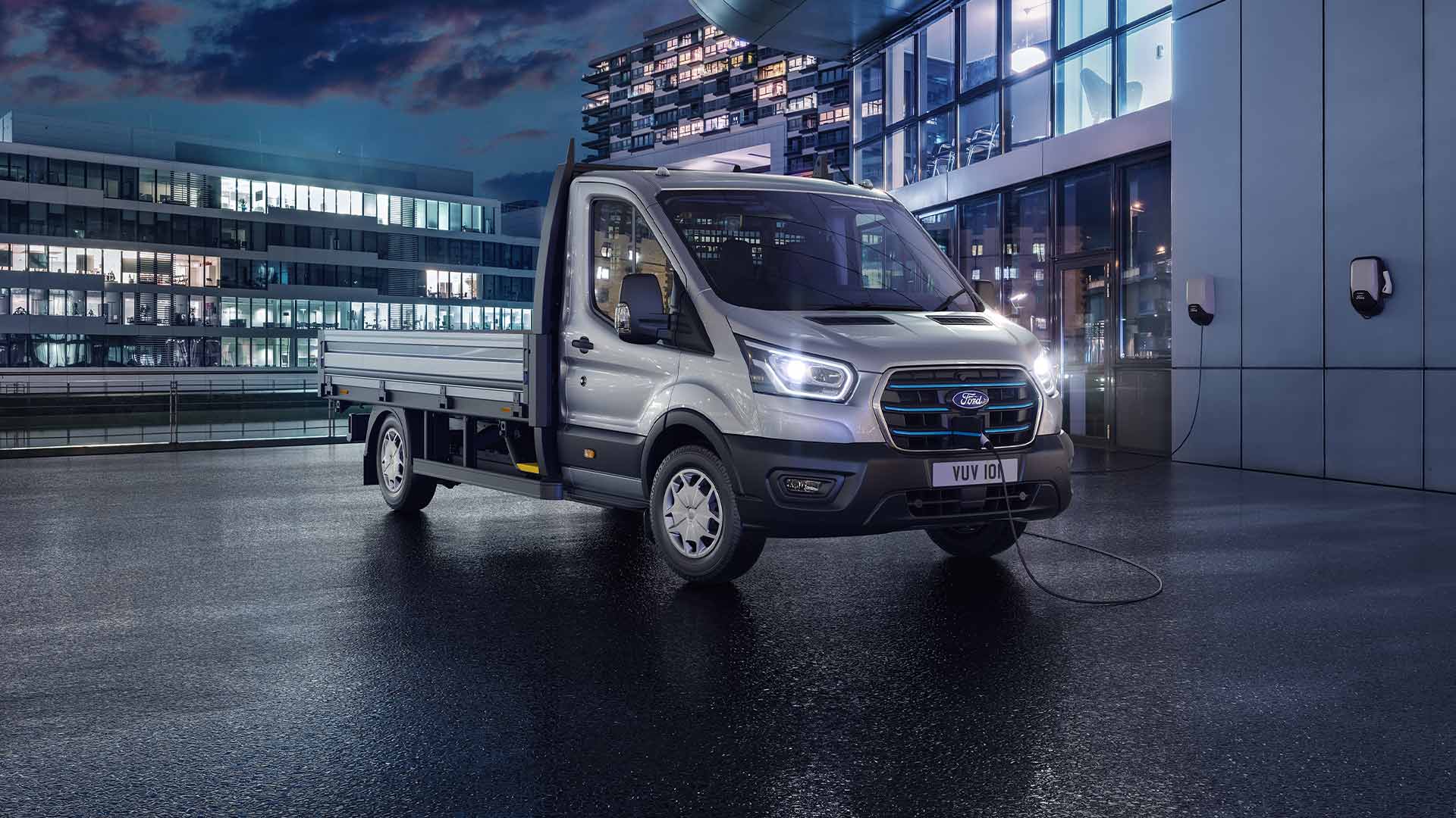 Silver Ford Transit chassis cab parked in front of a modern building at night.