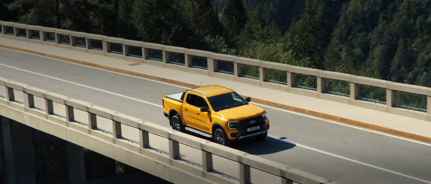 Ford Ranger Wildtrak driving on bridge near mountains 3/4 front view