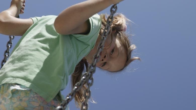  A child in a green t-shirt leans back on a swing against a clear blue sky, hair blowing in the wind.