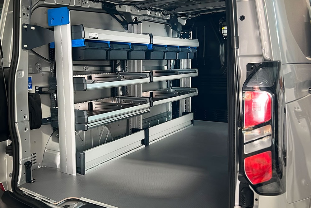 Rear interior of a Ford Transit van, showing a modular shelving system with various storage bins.