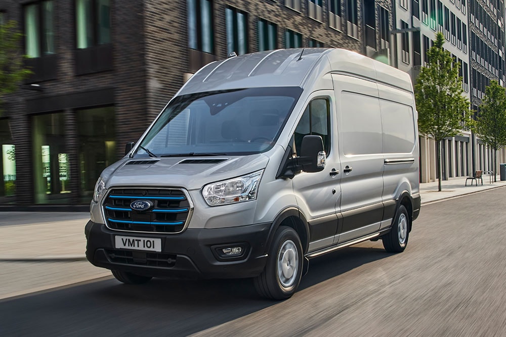 A silver Ford Transit driving through an urban landscape.
