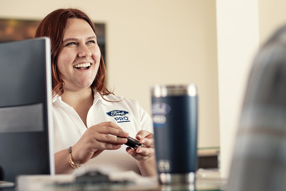 A Ford manager at her desk, smiling while talking with a customer.