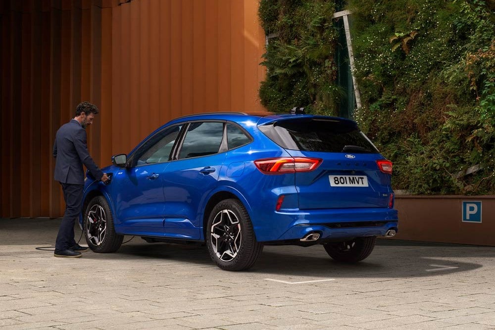 Man charging a parked blue Ford Kuga in an urban setting.