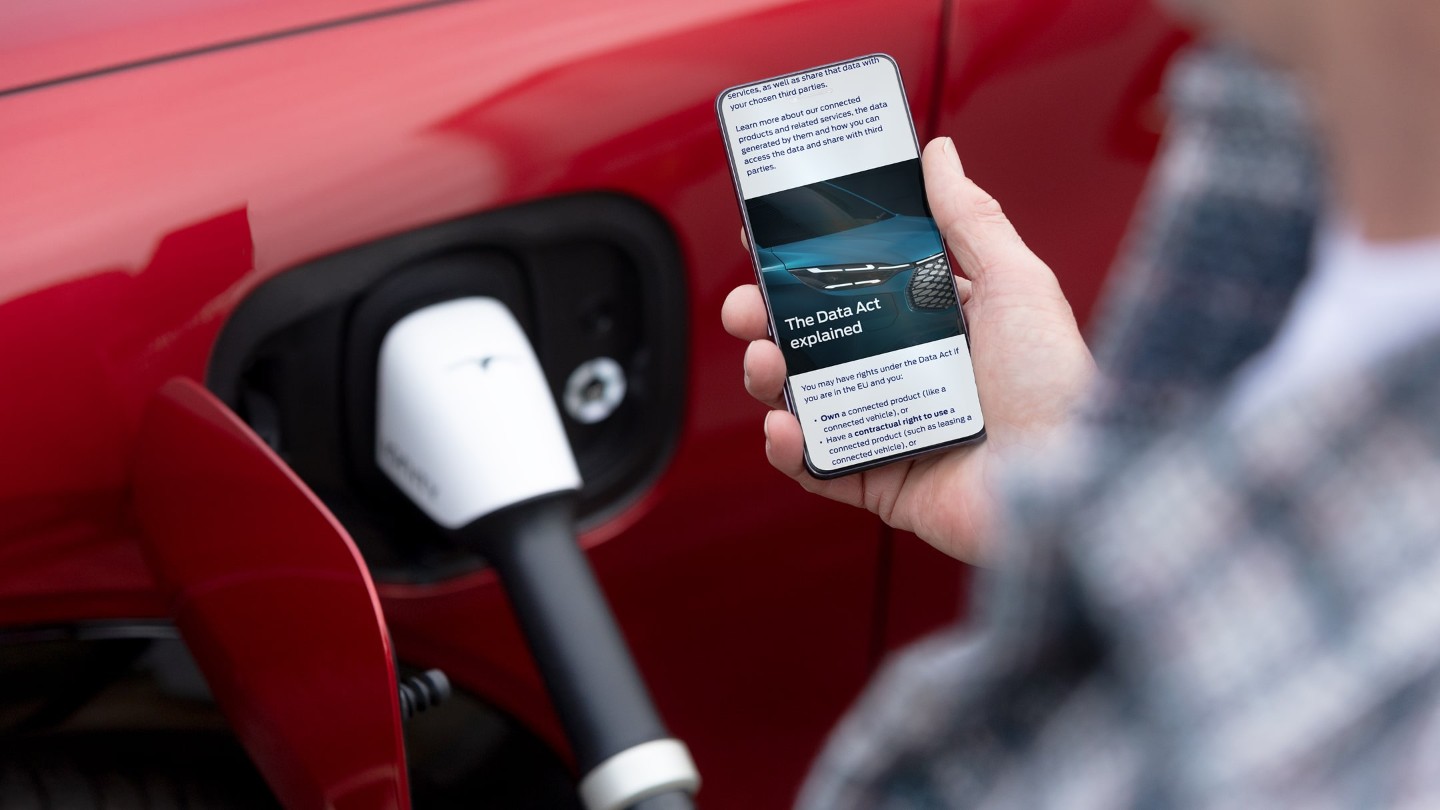 A person reading an explainer on the EU Data Act on their phone next to a charging electric vehicle.