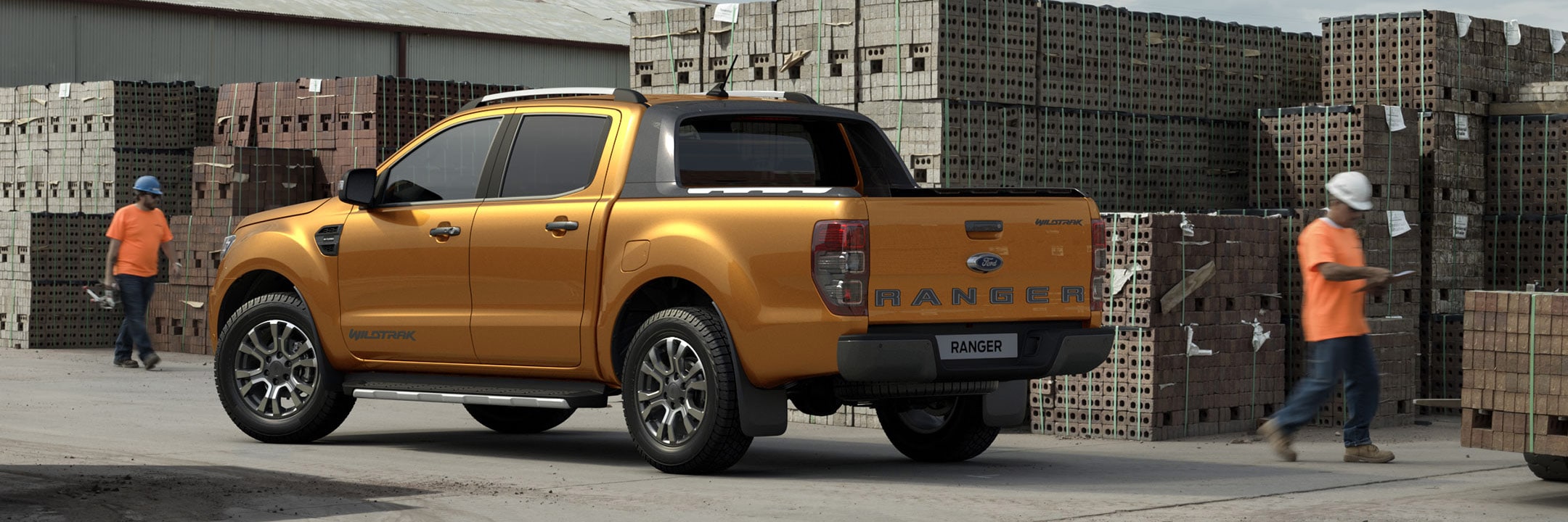 Rear shot of an orange Ford Ranger Wildtrak parked at a building site with two workers