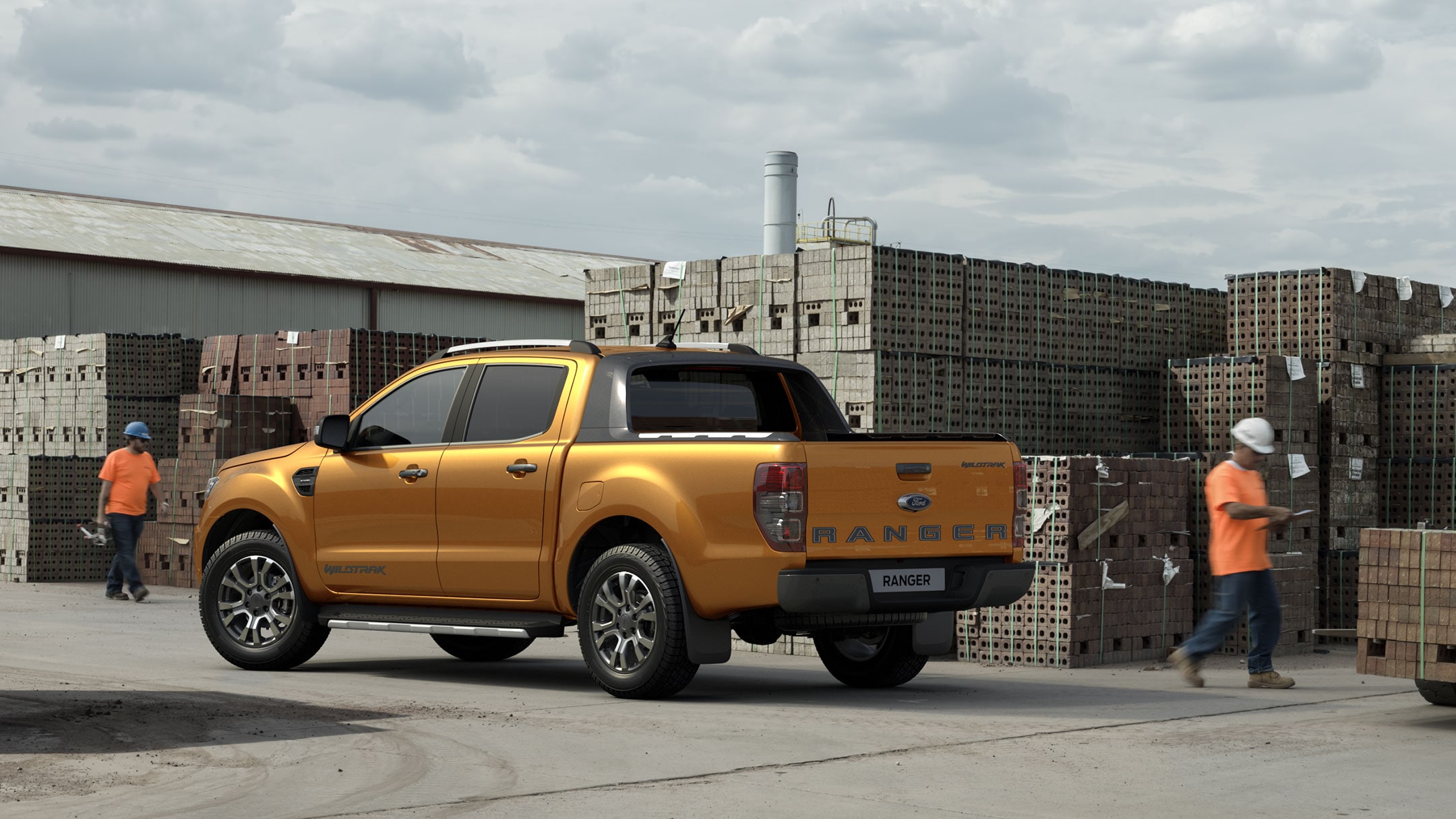 Rear shot of an orange Ford Ranger Wildtrak parked at a building site with two workers