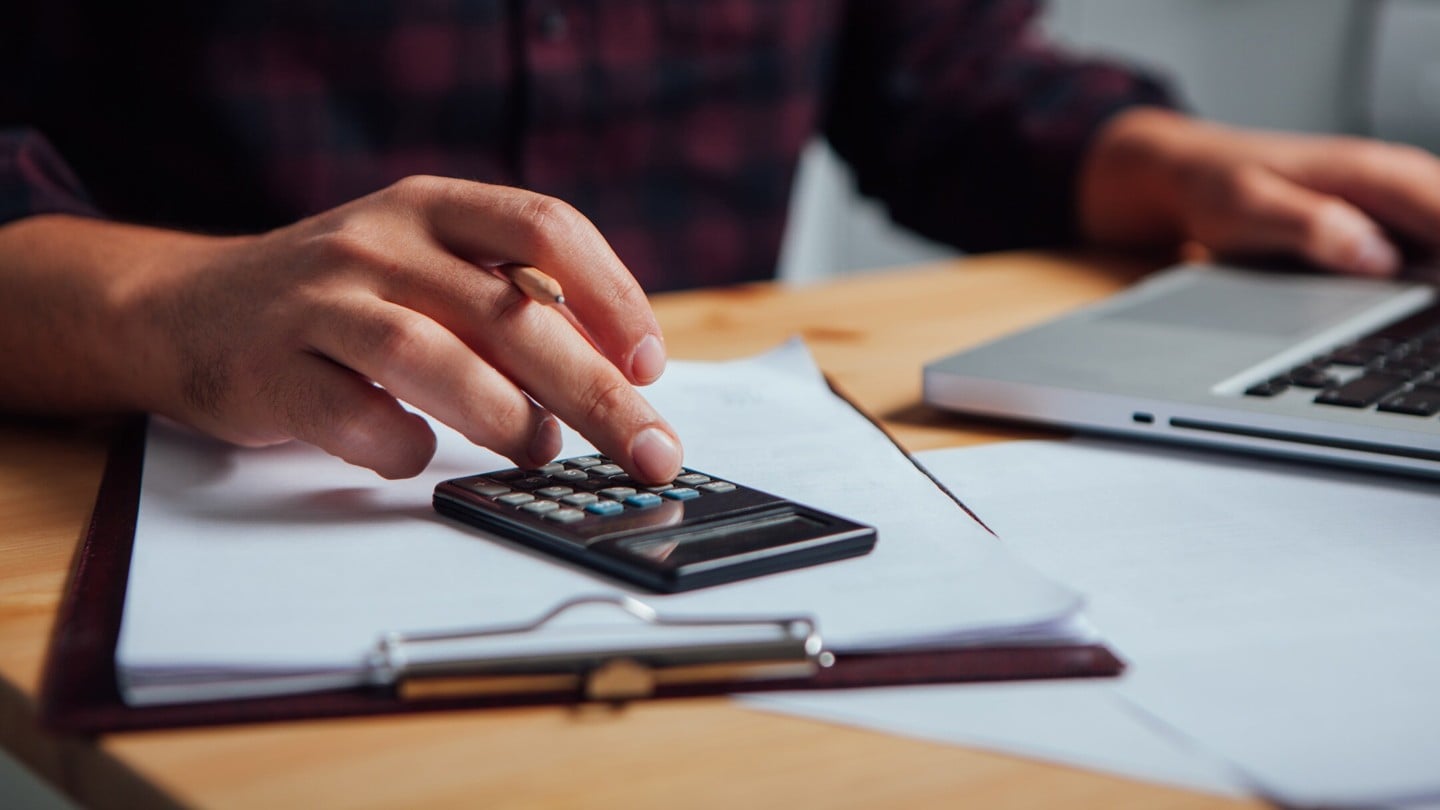 Close shot of a man's hand using a calculator and and a laptop